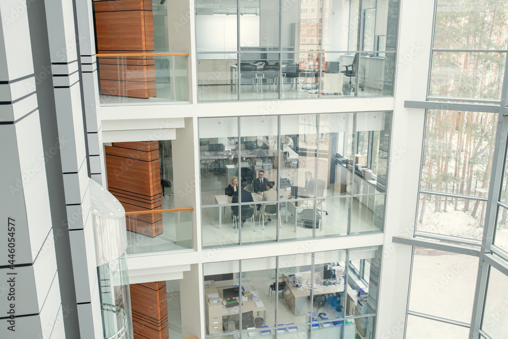 Poster image of modern office building with big windows and business people working together inside of it