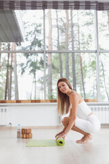 A barefoot woman twists green yoga mat and fitness on the parquet floor.