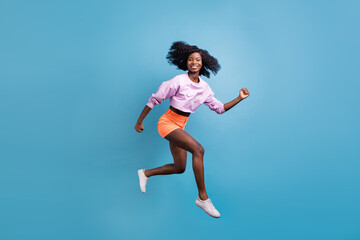 Full size profile side photo of young happy beautiful smiling afro girl running in air isolated on blue color background