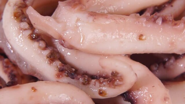 Squid or octopus tentacles in oil. Sea food, delicacy rotates as food background. Extreme macro view of sea tentacles of squid or cuttlefish.