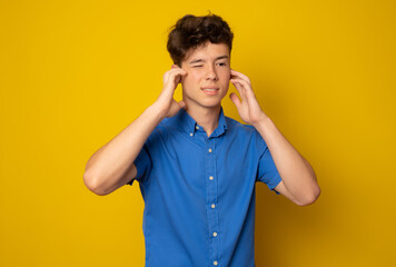 Boy covering his ears isolated over yellow background.