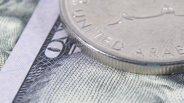 Stack of United Arab Emirates coins against the background of US hundred dollar bills. Pegged exchange rate concept. Macro view. Rotating money background. UAE money on american dollars. UAE exchange.