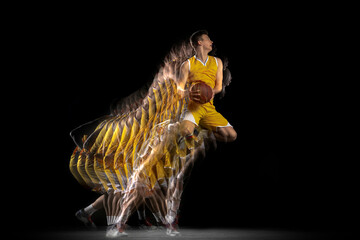 Power and speed. One young basketball player training with ball isolated on dark background with...