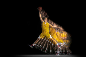 Power and speed. One young basketball player training with ball isolated on dark background with...