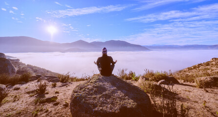 man meditating in lotus position on the mountains over the clouds