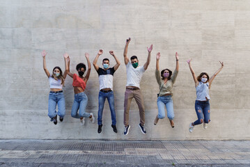 Young people with face masks jumping happy against a wall