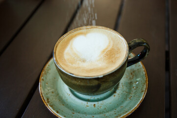 Sugar is poured into a cup of cappuccino. Cappuccino in a beautiful gray-green clay gull