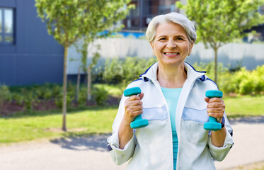 fitness, sport and healthy lifestyle concept - happy smiling senior woman with dumbbells exercising over city street background