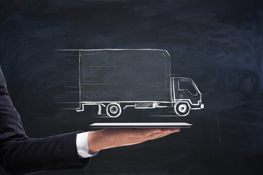 Businessman hand holding tablet with creative truck sketch. Transporation and logistics concept.