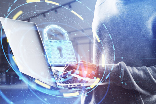 Close up of hacker hands using laptop with glowing padlock hologram on blurry office background. Online safety and attack concept. Double exposure.