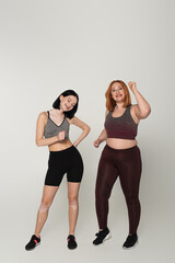 Body positive friends in sportswear dancing on grey background