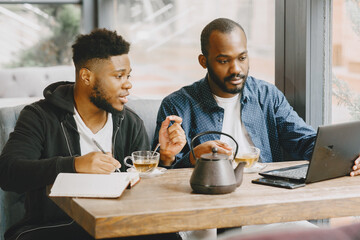 Two men sitting in a cafe and working behind a laptop and drink a tea.