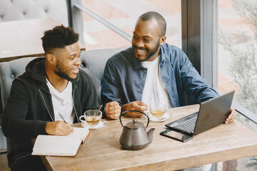 Two men sitting in a cafe and working behind a laptop and drink a tea.