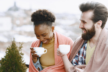 Man and woman on terrace in a blanket drinking coffee