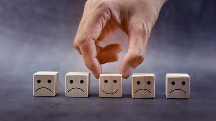 Closeup hands holding smiley face icon on wooden cube, service rating, leadership and corporate...