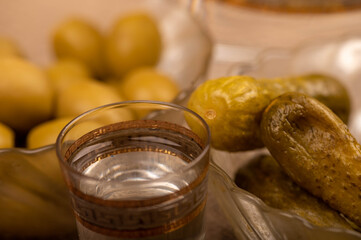 A glass of vodka and pickled cucumbers and salted olives in a glass dish on a background of homespun fabric with a rough texture. Close-up Selective focus.