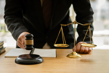 A lawyer working in an office and a judge's hammer and gold scales in front with a notebook on a legal advisor concept table.