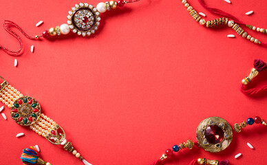 Raksha Bandhan, Indian festival with beautiful Rakhi and  Rice Grains on red background.  A traditional Indian wrist band which is a symbol of love between Sisters and Brothers.