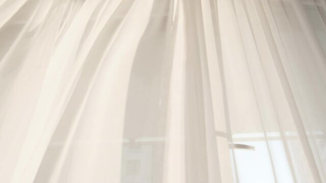 Transparent white curtain tulle moves from the wind from an open window. Sunny day, the sun's rays sunlight.