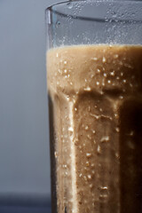 Cha Yen Thai iced tea brown-coloured in a glass, a half of glass on grey background front view