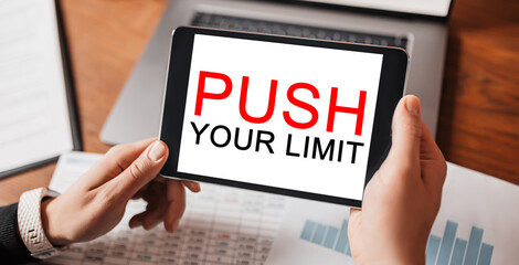 Man hands holding tablet with text PUSH YOUR LIMIT at workplace. Businessman working at desk with documents