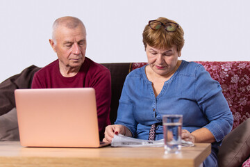 Aged couple going about their business, woman reading a newspaper and man opened laptop and sitting near his wife.