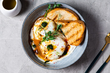 Cilbir or Turkish Eggs. dish served as mezze: poached eggs topped over herbed greek yogurt, then drizzled with hot spiced paprika olive oil. Turkish breakfast in a grey bowl on marble background
