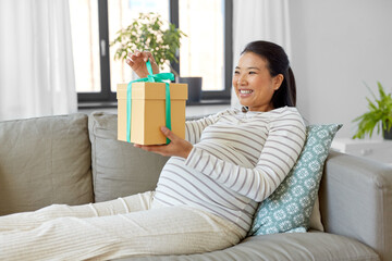 pregnancy, holidays and people concept - happy smiling pregnant asian woman with gift box sitting on sofa at home