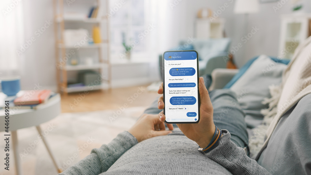 Wall mural man at home lying on a couch and using smartphone for chatting with his girlfriend, arranging a date