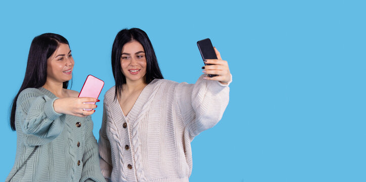 Two beautiful sisters girl with makeup and hairdo are making selfie holding the cellphones in their hands. 