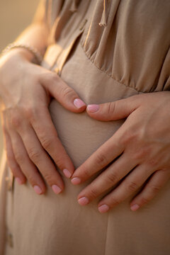 a pregnant woman in a beige dress holds a hand on a tummy. Waiting for a baby, pregnant photo session. pregnancy and childbirth in the summer, 9 months. motherhood concept