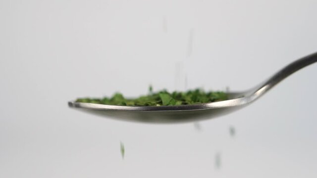 Fill a metal spoon with dried parsley spice. Sprinkle seasoning in a slow motion. Macro. On white background