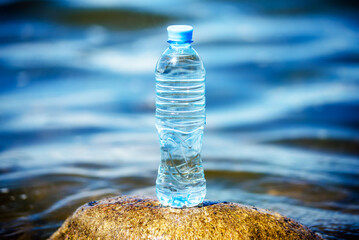A bottle of drinking water stands on a stone on the seashore
