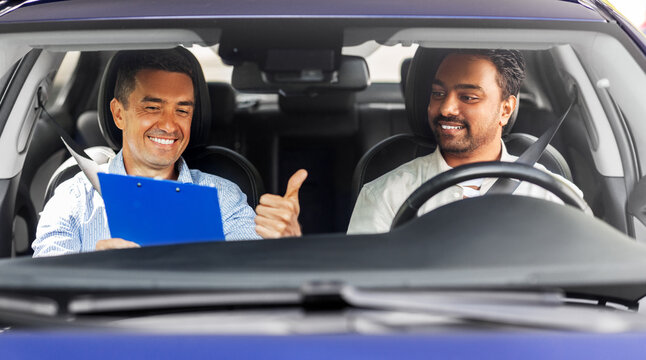 driver courses, exam and people concept - happy smiling indian man and driving school instructor with clipboard showing thumbs up in car