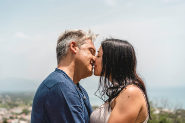 Authentic happy couple with beautiful woman and cool man kissing against a sea landscape during the summer vacation - People, love and tourism concept