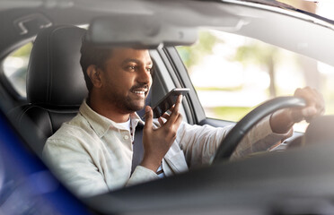 transport, people and technology concept - smiling indian man or driver driving car and recording message using voice command recorder on smartphone