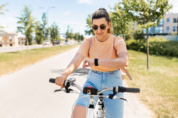 people, leisure and lifestyle - happy smiling young woman with smart watch riding bicycle on city street