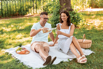 leisure and people concept - happy couple having picnic and pouring wine to glass at summer park