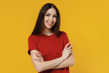 Obraz premium Smiling happy overjoyed beautiful vivid young brunette woman 20s wear basic red t-shirt hold hands crossed look camera isolated on yellow background studio portrait. People emotions lifestyle concept