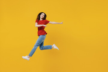 Fototapeta na wymiar Full size body length young brunette woman 20s wears basic red t-shirt jump pointing back on workspace area copy space mock up isolated on yellow background studio portrait. People emotions concept