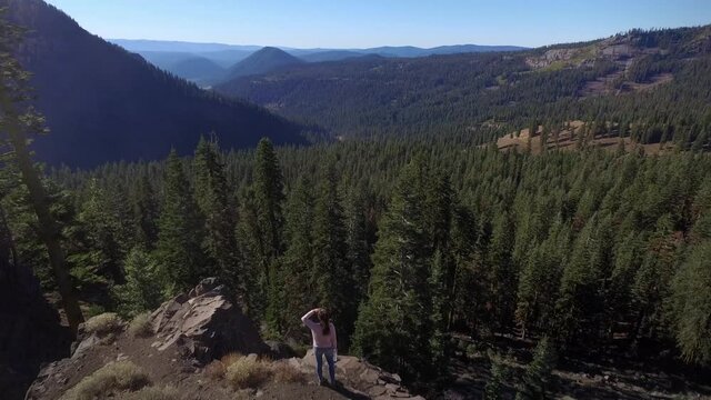 Aerial Drone view of woman looking out over a ridge in a pine forest in california