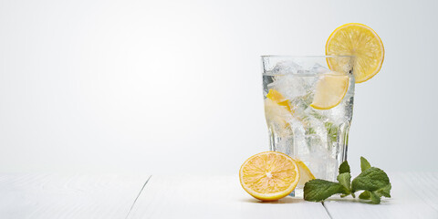 Glass of water with fresh lemons, leaves of mint and ice cubes on light background. Homemade refreshing lemonade, lemon drink.