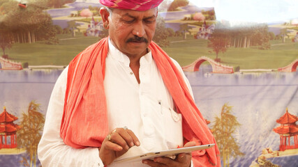 Portrait of a middle-aged Indian male with a mustache and pink turban looking at a tablet