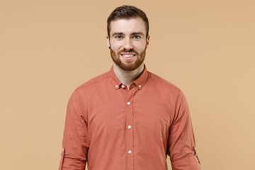Smiling happy handsome tatooed young brunet man 20s short haircut with earrings wears apricot shirt look camera isolated on pastel orange background studio portrait. People emotions lifestyle concept