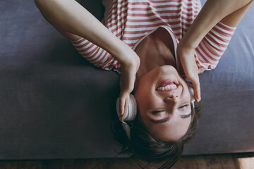 Close up side view young excited woman in casual clothes headphones lying on grey sofa listen to music calm melody antistress rest on weekends indoors flat at home. People lifestyle leisure concept