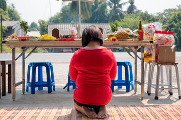 Asian woman red shirt sitting and praying to ancestor with meal,dessert and beverage on table in...