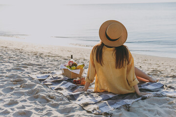Full length back rear view young woman wearing straw hat shirt summer clothes sitting on plaid have picnic outdoors on sea sunrise sand beach background. People vacation lifestyle journey concept