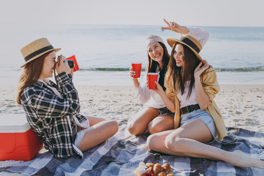 Full size three friends fun young women in straw hat summer clothes have picnic hang out take photo drink liguor glasses raise toasts outdoors on sea beach background People vacation journey concept.
