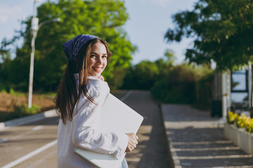 Side view fun young traveler tourist woman in blue bandana shirt summer casual clothes rest holding closed laptop pc computer walk go down park alley outdoors People urban lifestyle journey concept.