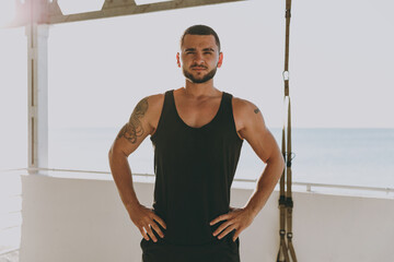 Fototapeta na wymiar Young strong sporty athletic toned fit sportsman man in sports clothes warm up training with TRX work out hold hands on waist at sunrise sun dawn over sea beach seaside outdoor in summer day morning